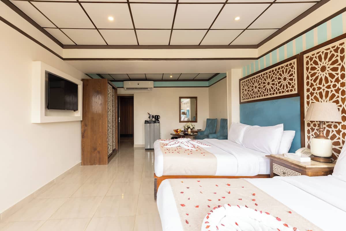 A hotel room with two beds, a TV, a desk, a chair, and a decorative wall panel.