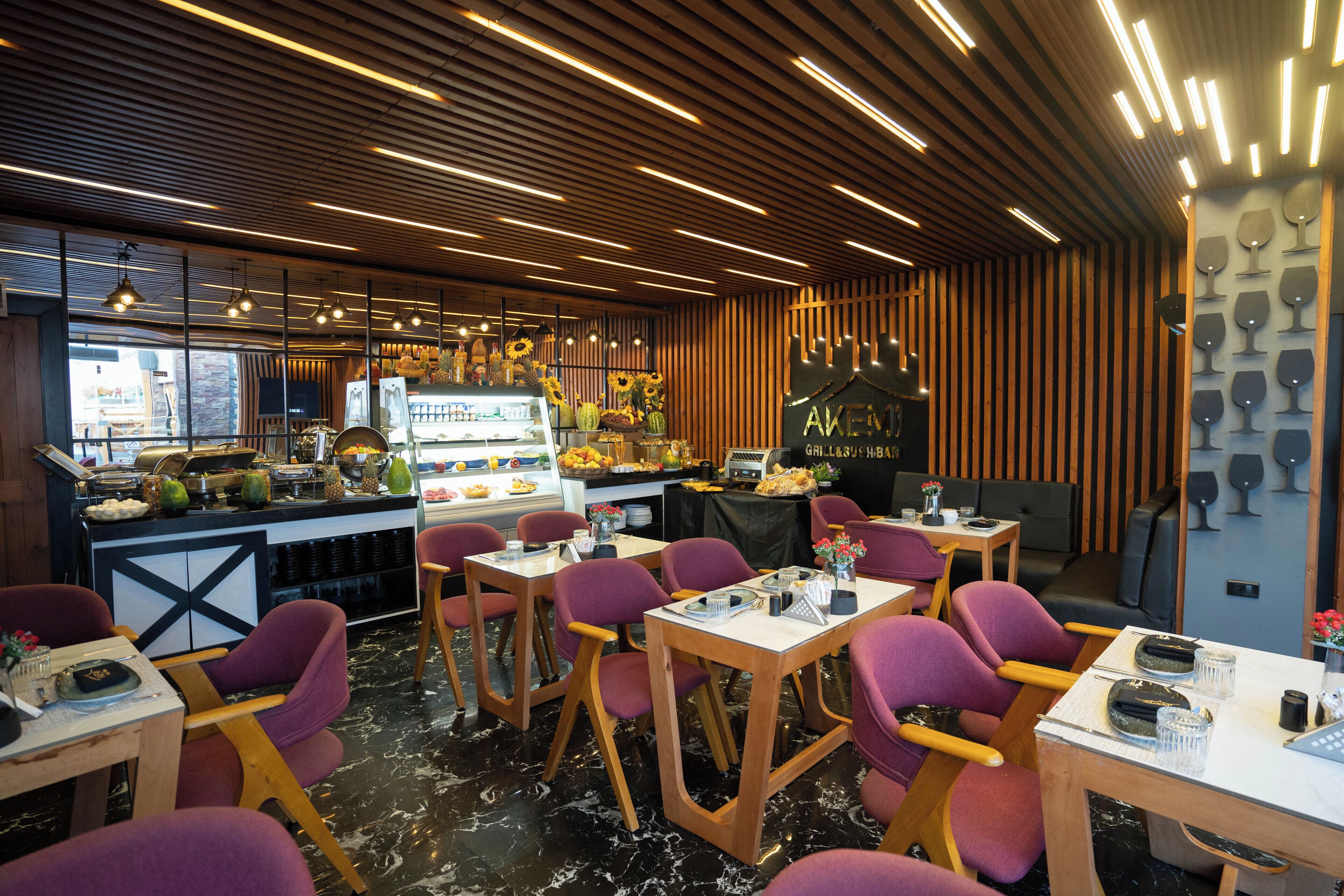 Interior de un restaurante con techos de listones de madera, sillas moradas y una exhibición de copas de vino.