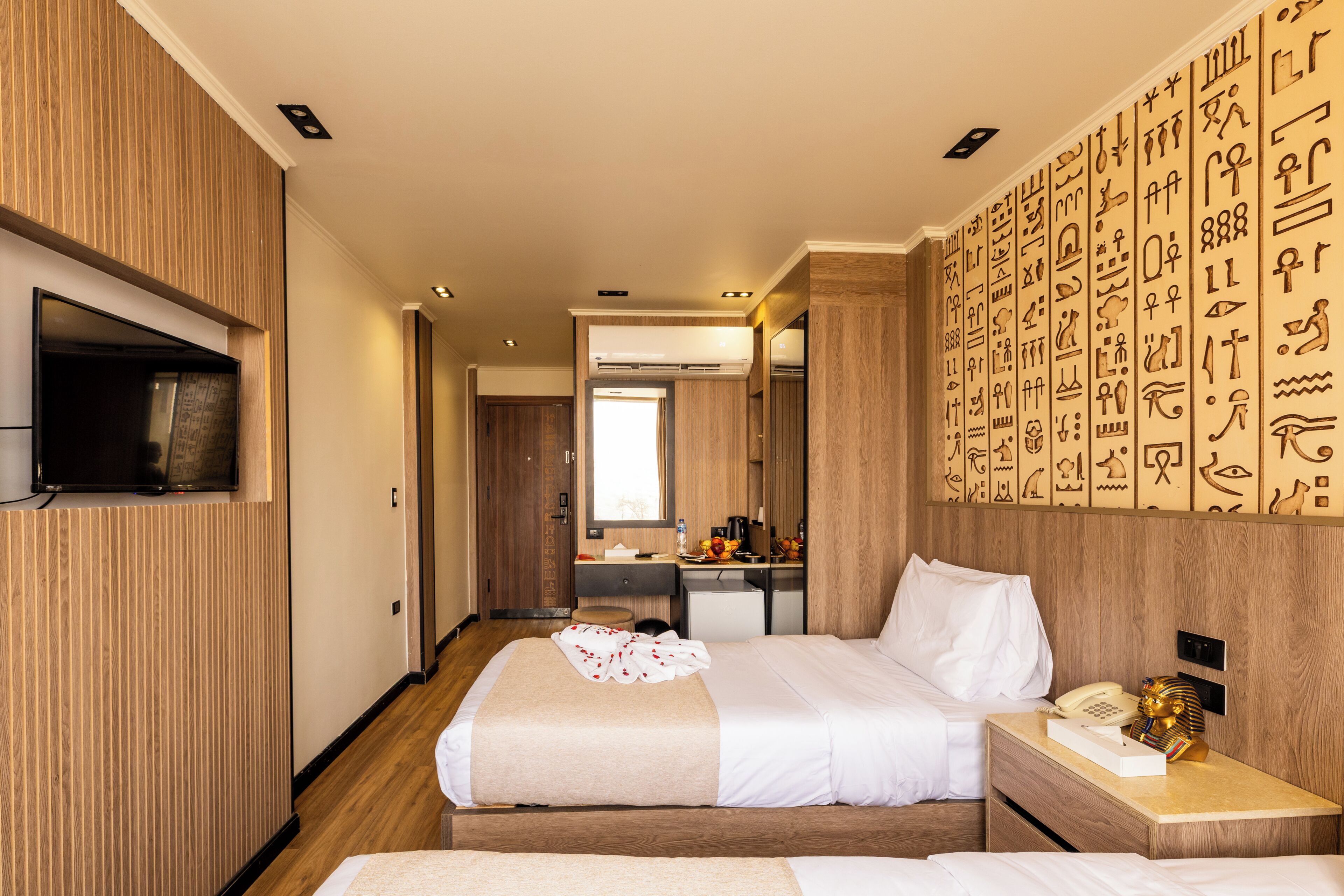 A hotel room with a bed, bedside table, and a wall with hieroglyphs.