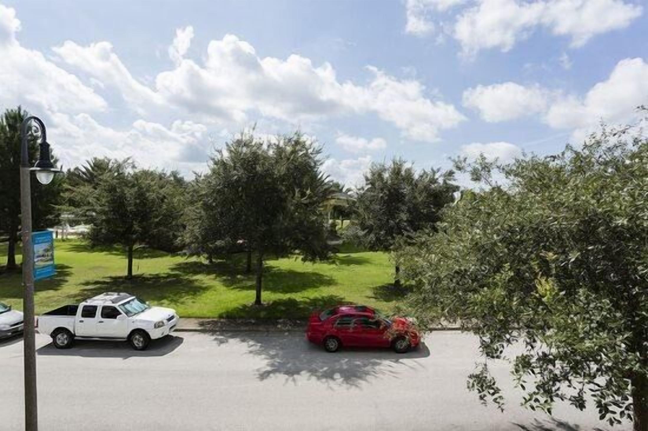 Une vue d’une rue avec un camion blanc garé sur le bord, une voiture rouge stationnée dans la rue et un lampadaire.