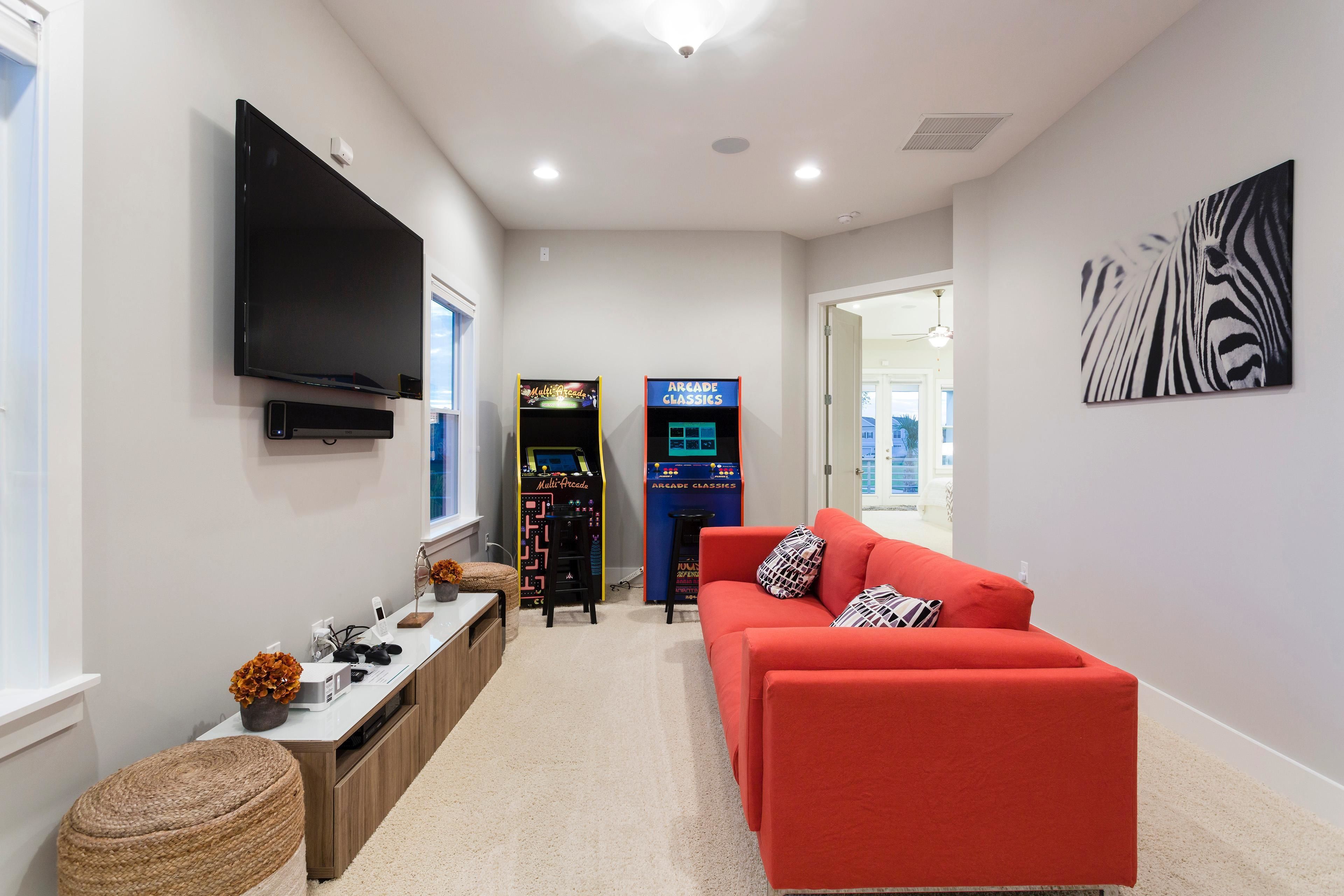 A modern living room with a flat-screen TV, a red sofa, arcade game machines, and a zebra artwork on the wall.