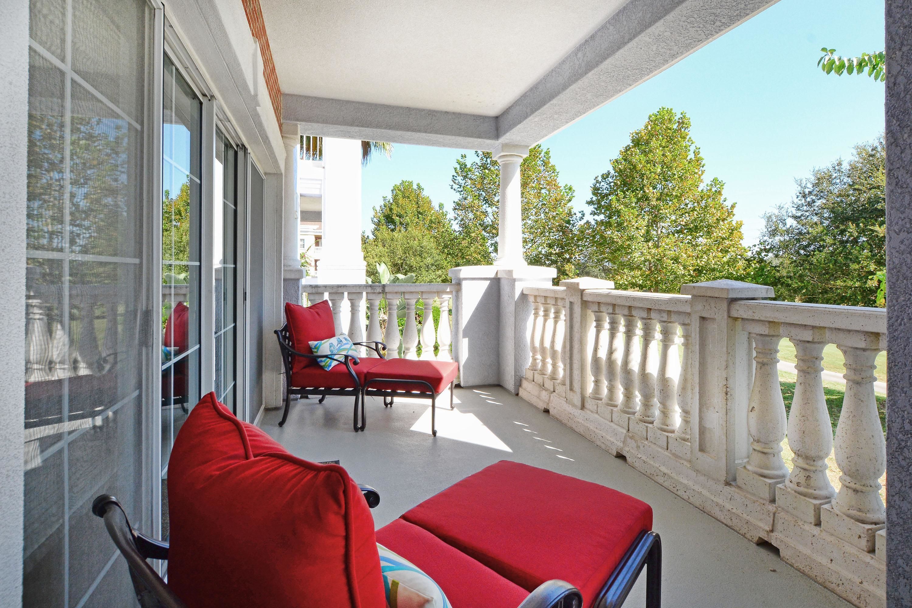 Un balcon avec des fauteuils à coussins rouges et une table, donnant sur un jardin.