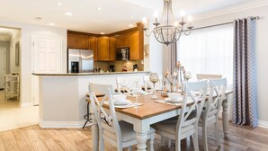 A modern kitchen with wooden cabinets, stainless steel appliances, and a dining area with a wooden table and white chairs. - Condo Serenity at Cabana Court 3 Bedroom Reunion (Kissimmee)