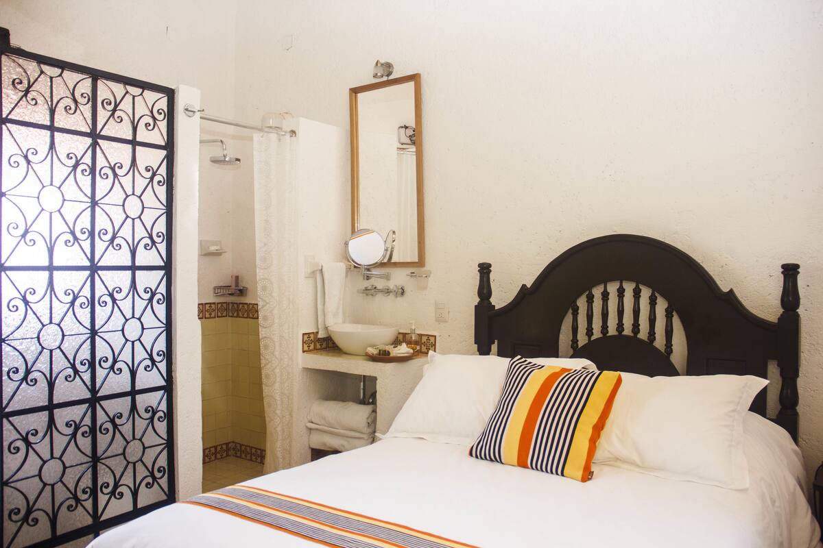 Een slaapkamer met een bed, nachtkastje, spiegel en douche.