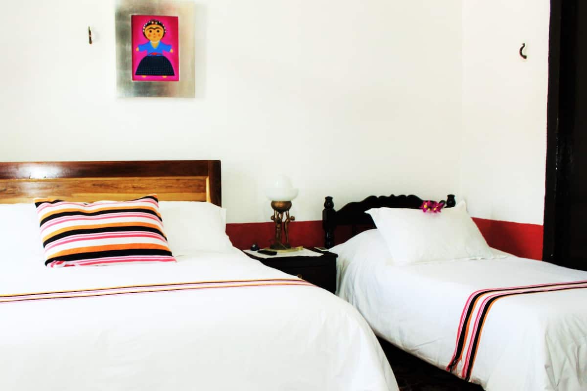 Een hotelkamer met twee bedden, elk voorzien van witte beddengoed en gestreepte kussens. Er is een houten hoofdbord, een nachtkastje met een lamp, en een ingelijst beeld op de muur.