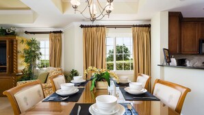 A dining room with a large table set for four, surrounded by chairs, with a chandelier above and curtains on the windows. - Condo Centre Court Sun 3 Bedroom Reunion (Kissimmee)