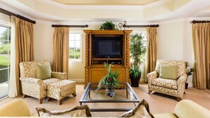 A living room with two patterned armchairs, a glass coffee table with a plant, a television on a wooden stand, and a ceiling fan. - Condo Centre Court Sun 3 Bedroom Reunion (Kissimmee)
