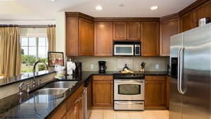 A kitchen with wooden cabinets, stainless steel appliances, a double sink, and a window with curtains. - Condo Centre Court Sun 3 Bedroom Reunion (Kissimmee)