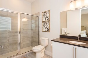 A modern bathroom with a glass shower enclosure, a toilet, a sink with a mirror, and two wall-mounted decorative panels.