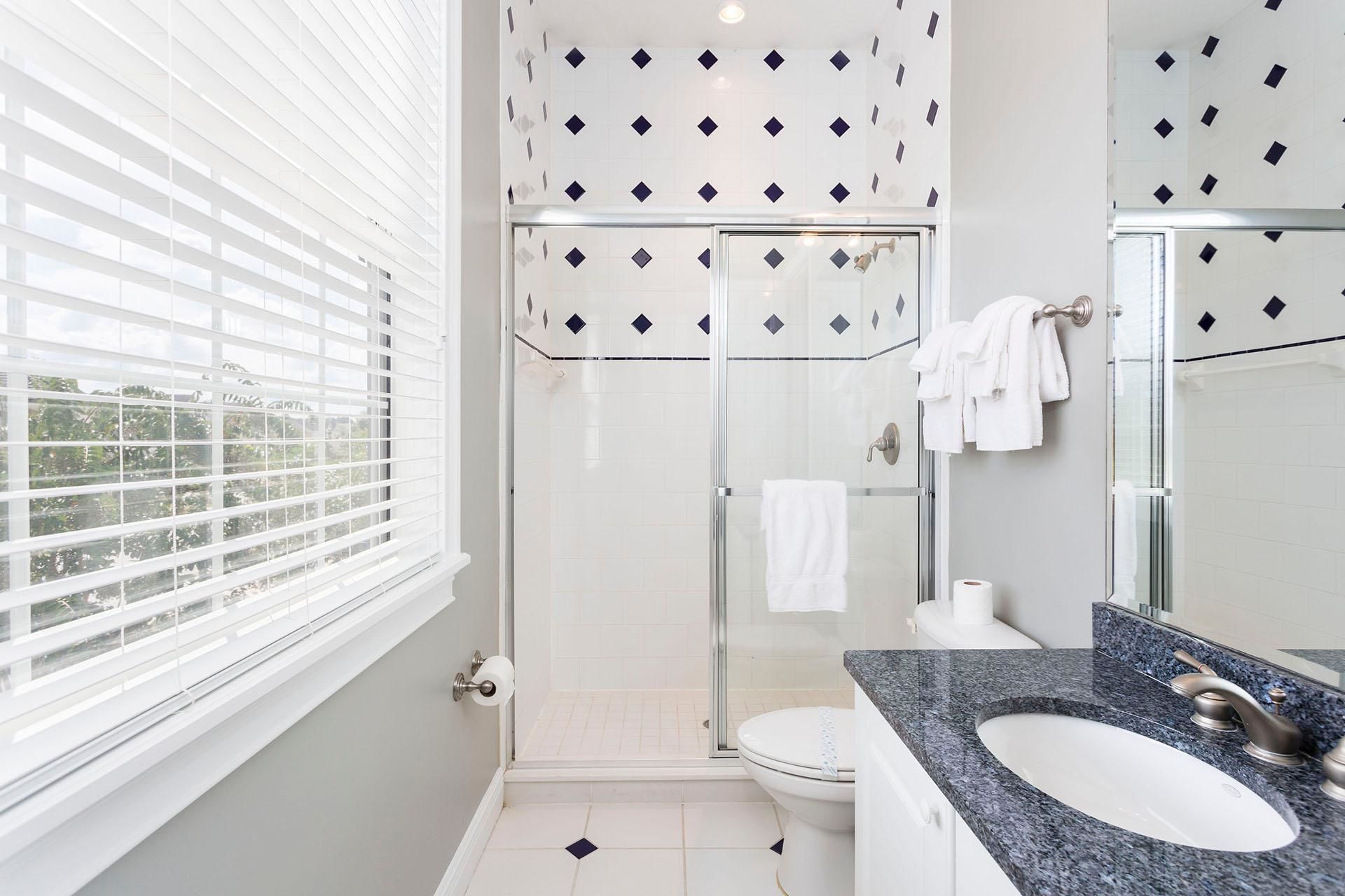 A modern bathroom with a glass shower enclosure, a white toilet, and a granite countertop sink.