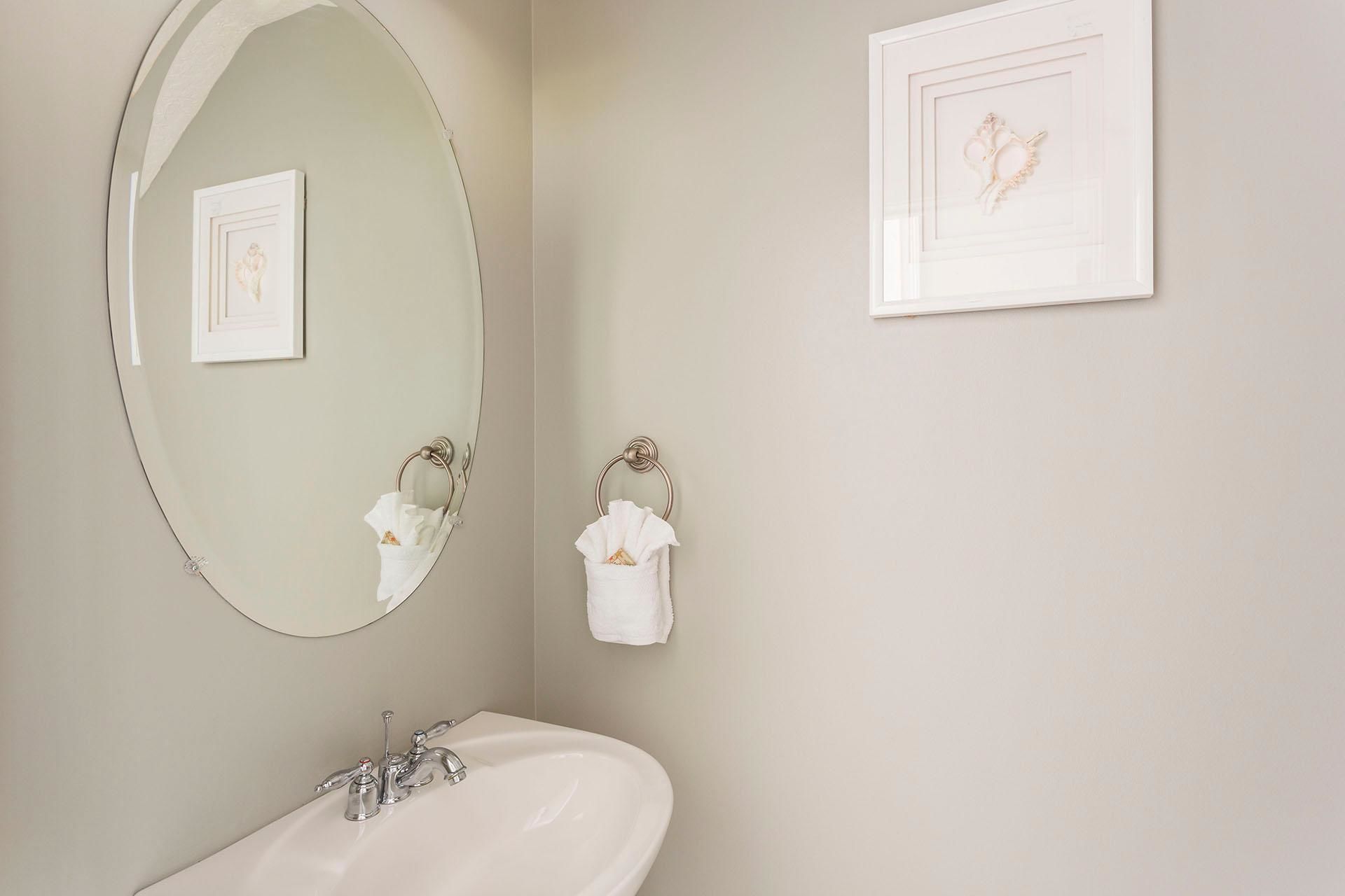 Une salle de bain avec un grand miroir ovale, un lavabo avec un seul robinet et deux serviettes suspendues à des porte-serviettes.