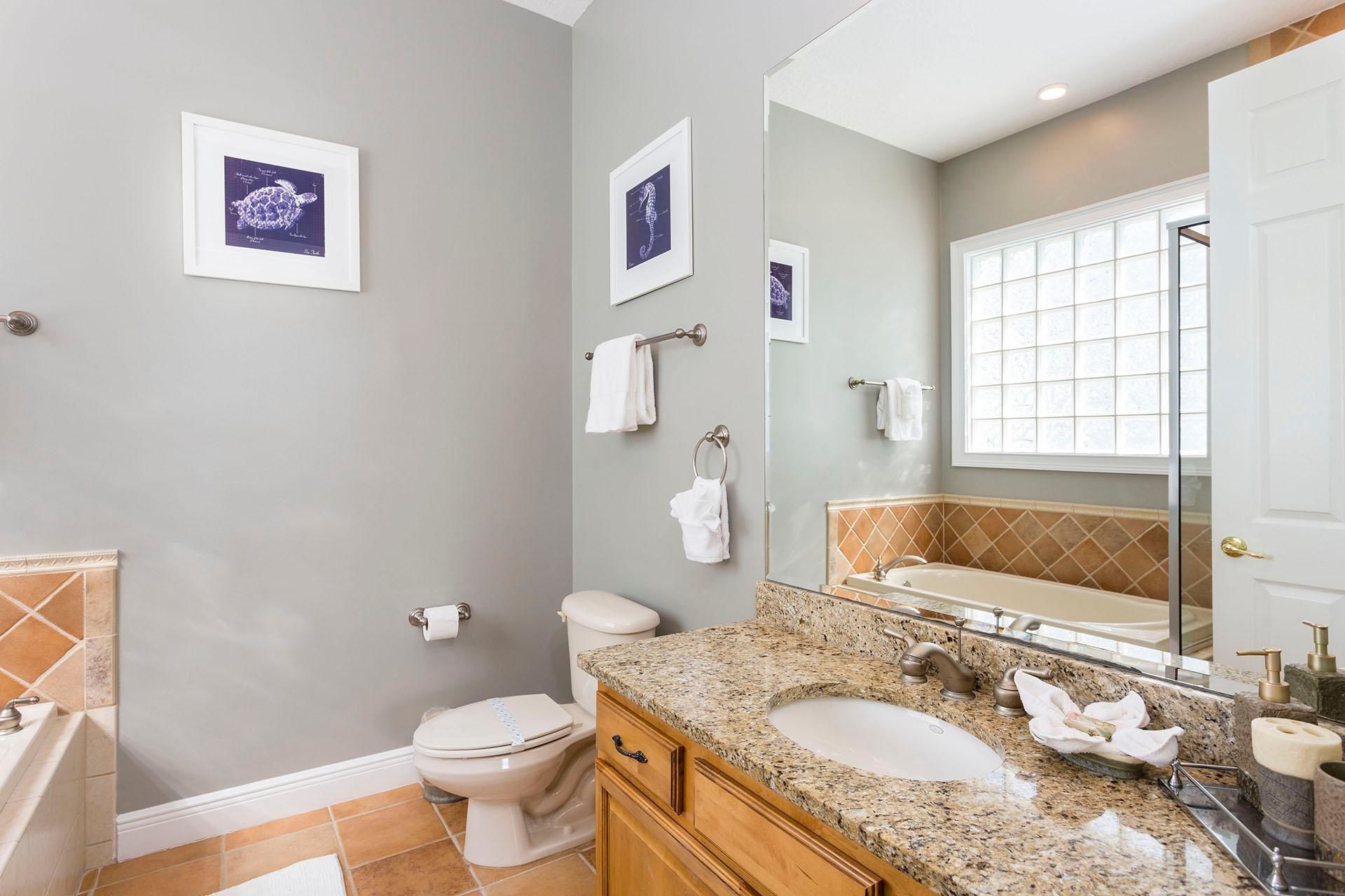A bathroom with a toilet, sink, and bathtub. There are framed pictures on the wall and a large mirror above the sink.