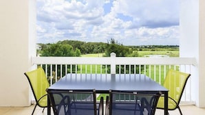 A balcony with a table and chairs, offering a view of a green landscape and a cloudy sky. - Condo Hertitage Crossing Modern Delight 3 Bedroom Reunion (Kissimmee)