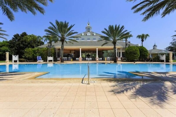 A swimming pool with a building in the background, palm trees, and a clear sky.