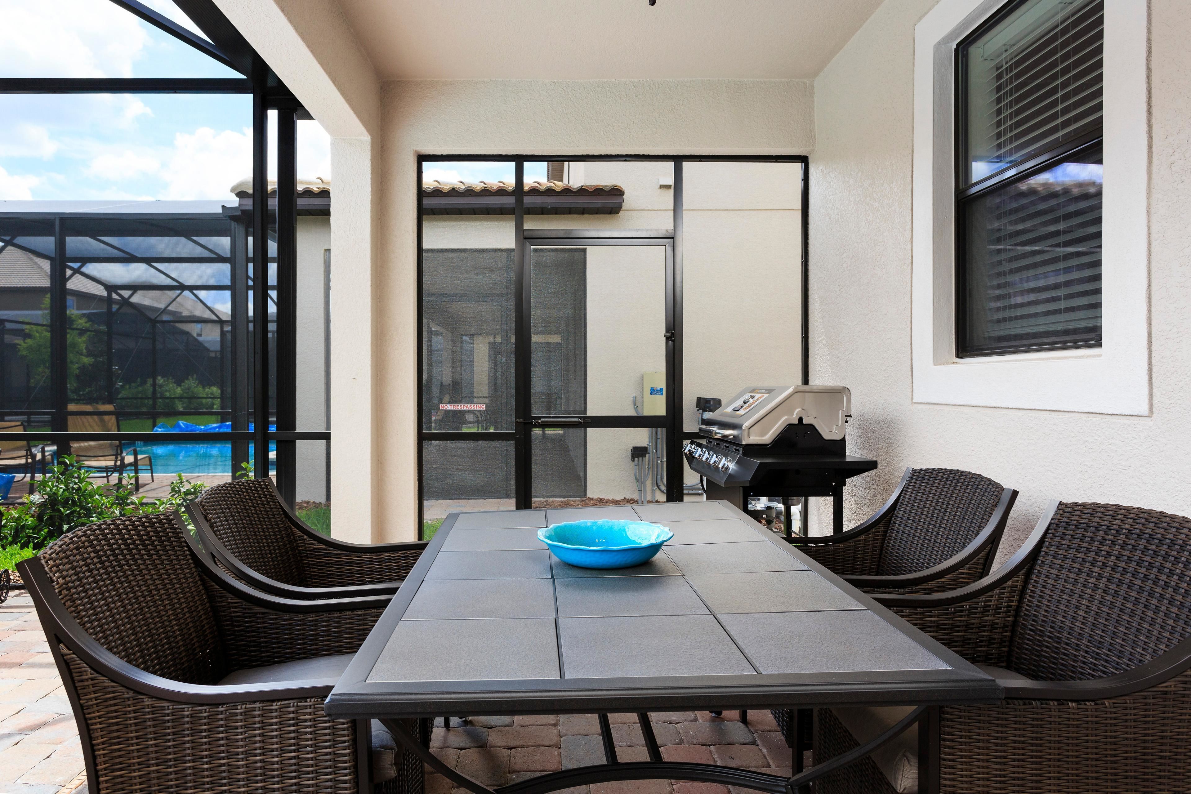 Un patio al aire libre con una mesa, sillas, una parrilla y vista a una piscina.