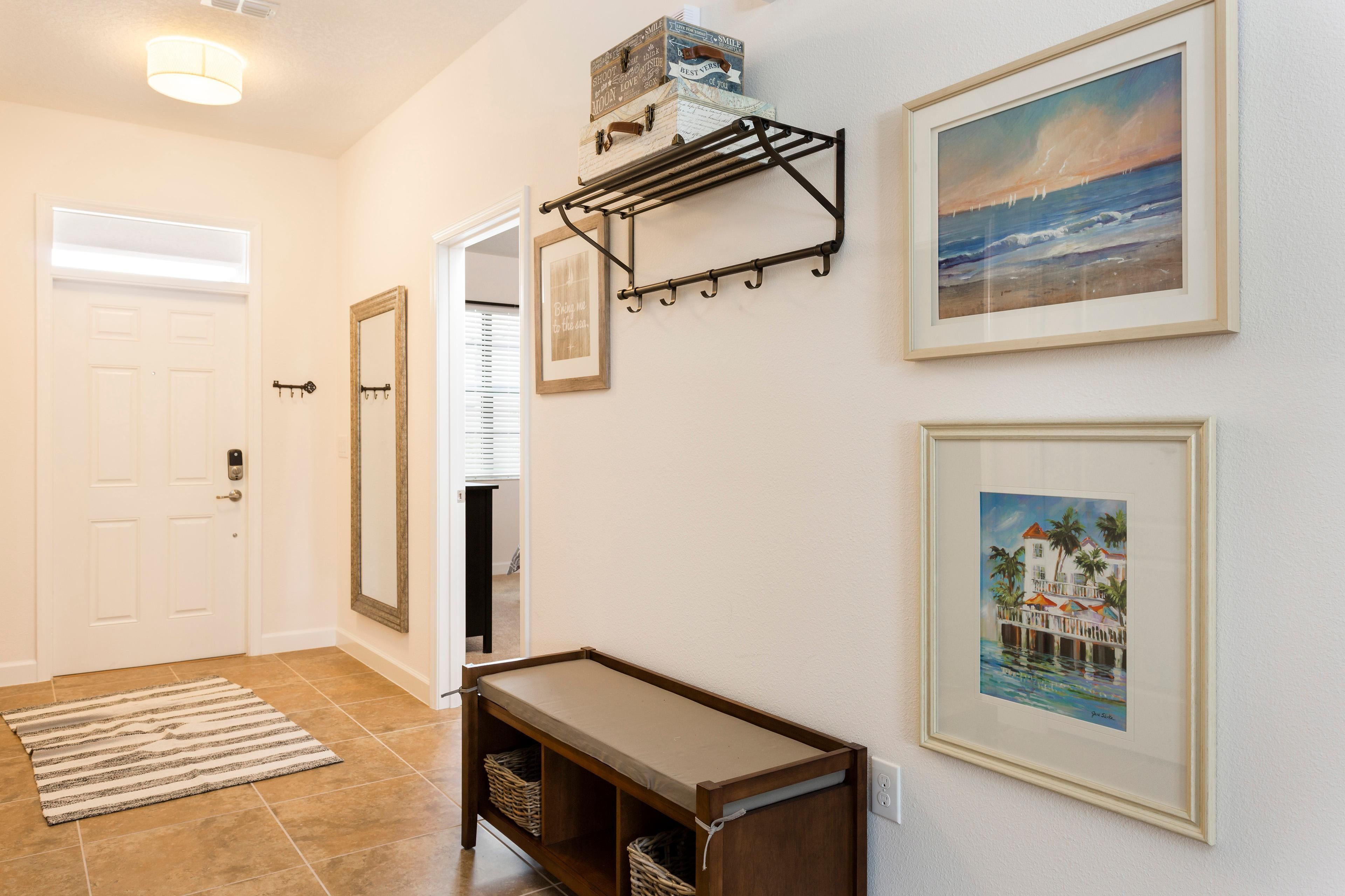 A hallway with a wooden bench, a wall-mounted shelf, and framed artwork.