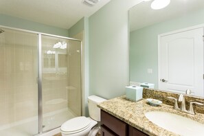 Une salle de bain avec une douche à parois de verre, des toilettes, un lavabo avec un plan de travail en granit et un miroir au-dessus du lavabo.