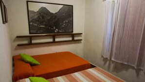 A small, single-bed room with an orange bedspread, a striped pillow, and a framed picture of a mountainous landscape on the wall. - Casa Rural Sofia (Hermigua)