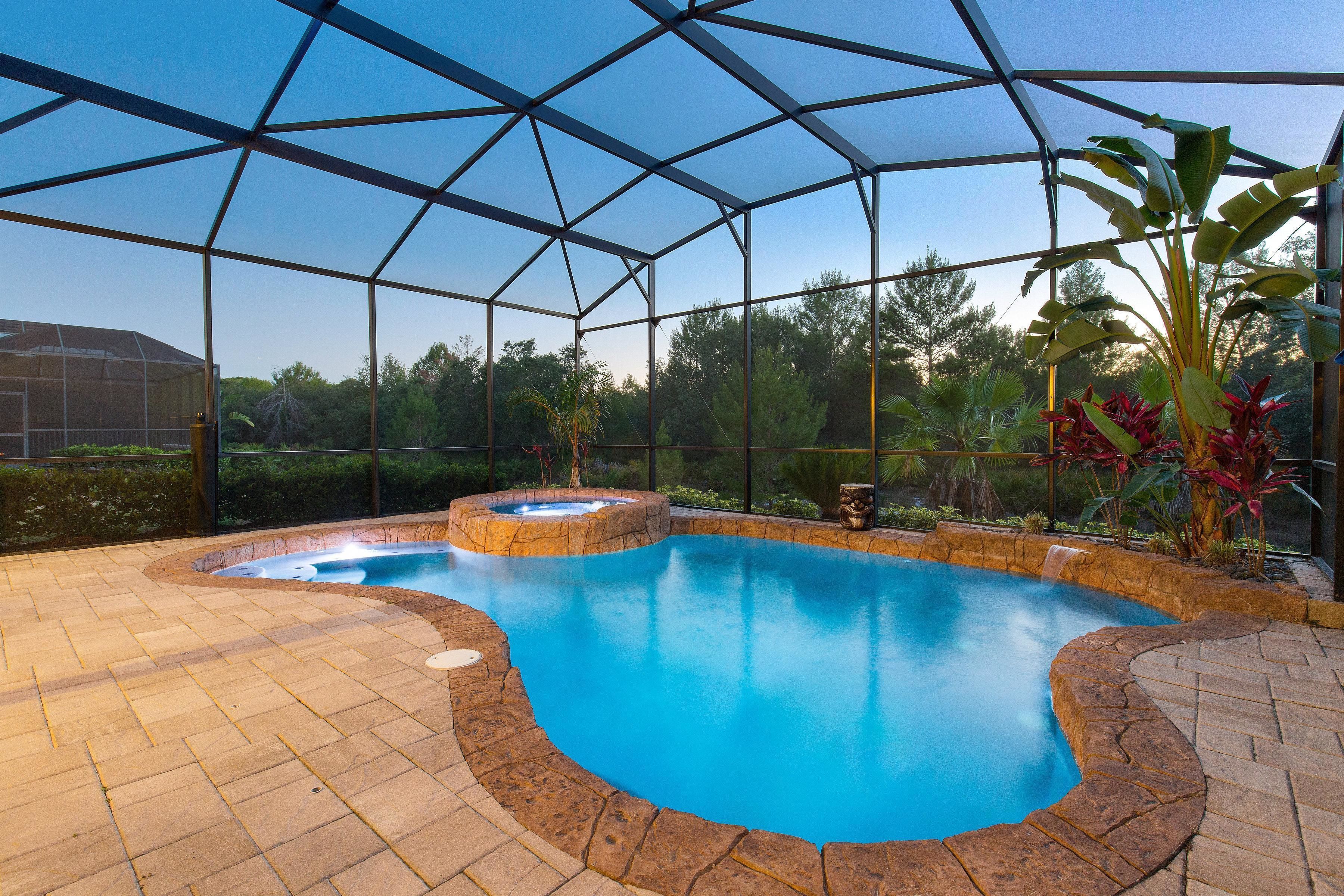 A swimming pool with a hot tub, surrounded by a glass enclosure and stone tiles.