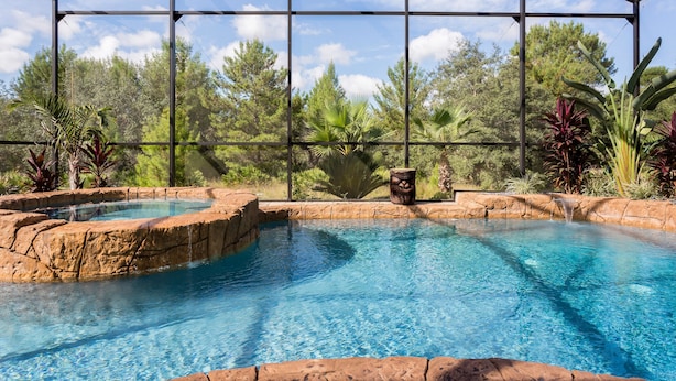 Una piscina de agua cristalina azul, rodeada por una barandilla de roca y plantas tropicales, bajo una estructura de techo metálico.