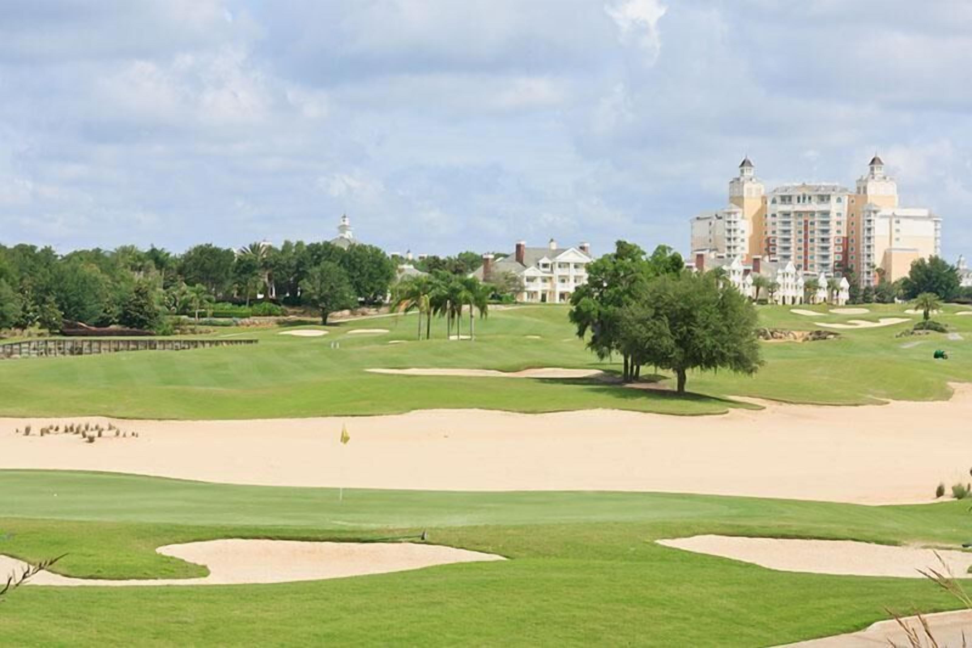 A golf course with sand bunkers, a clubhouse, and a large hotel in the background.