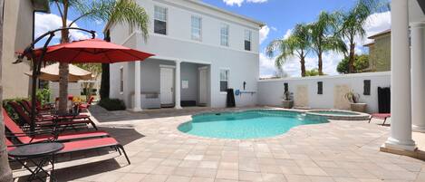 A pool area with lounge chairs and umbrellas, a white building with columns, and palm trees.