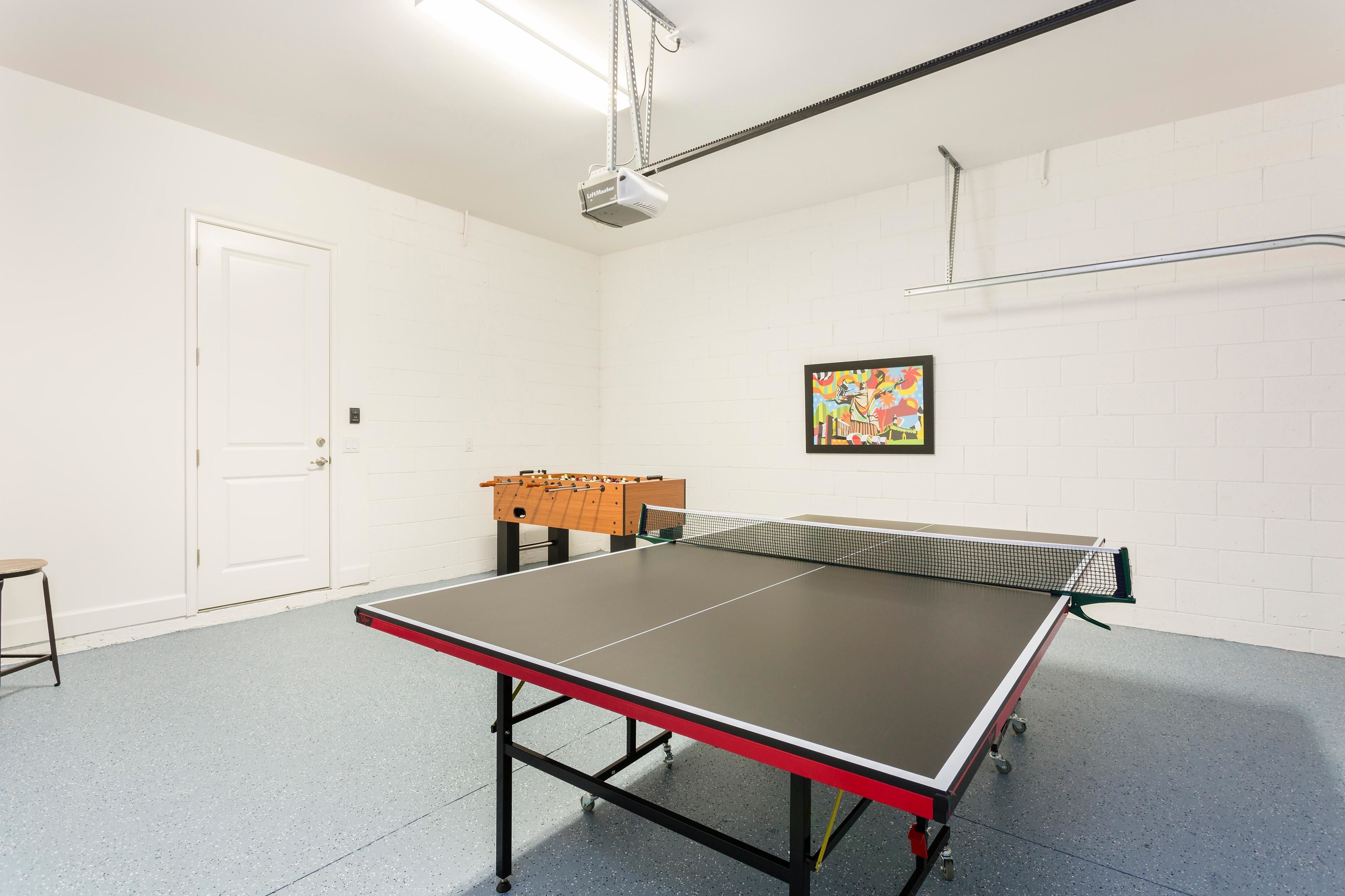 Mesa de ping pong en una habitación con paredes de ladrillo blanco, una puerta y un proyector montado en el techo.