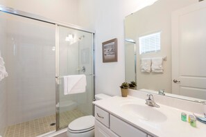 Een moderne badkamer met een glazen douchecabine, een witte wastafel en een grote spiegel.