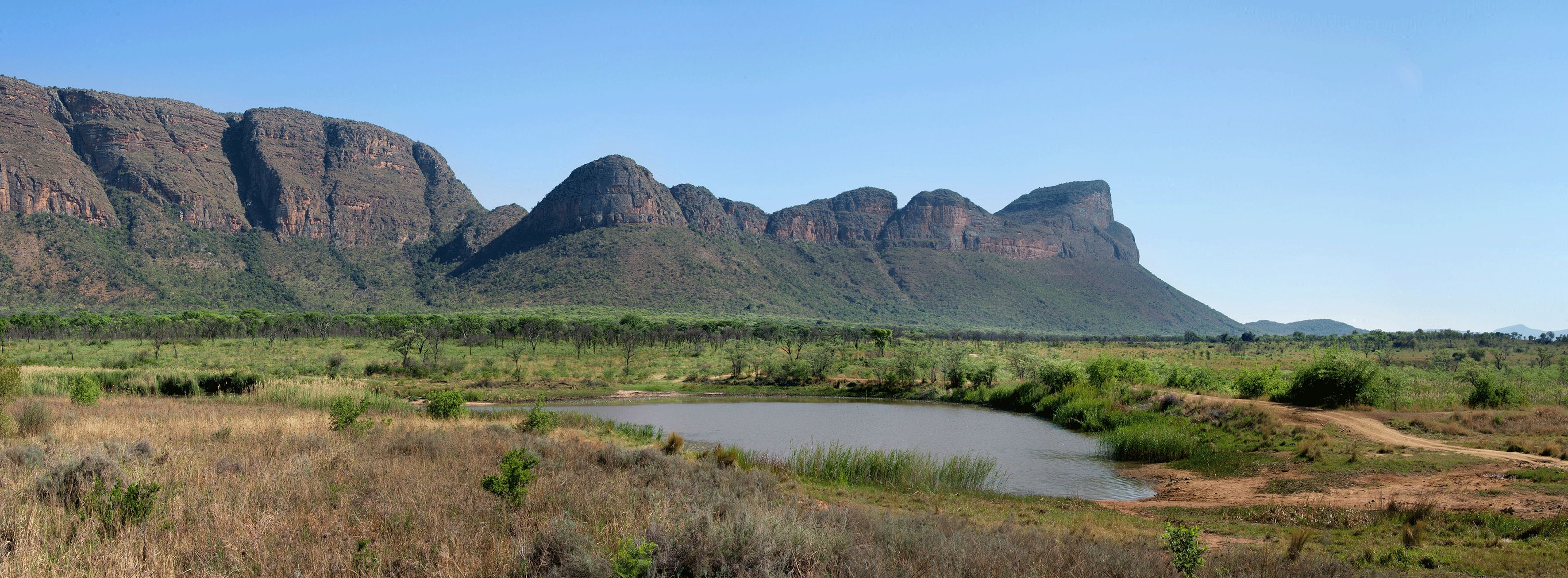 A natural landscape with a river, green vegetation, and mountains in the background.
