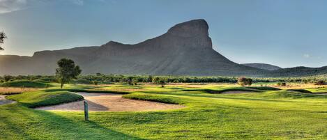 Un campo de golf con extensas zonas verdes, bunkers de arena y una montaña destacada al fondo.