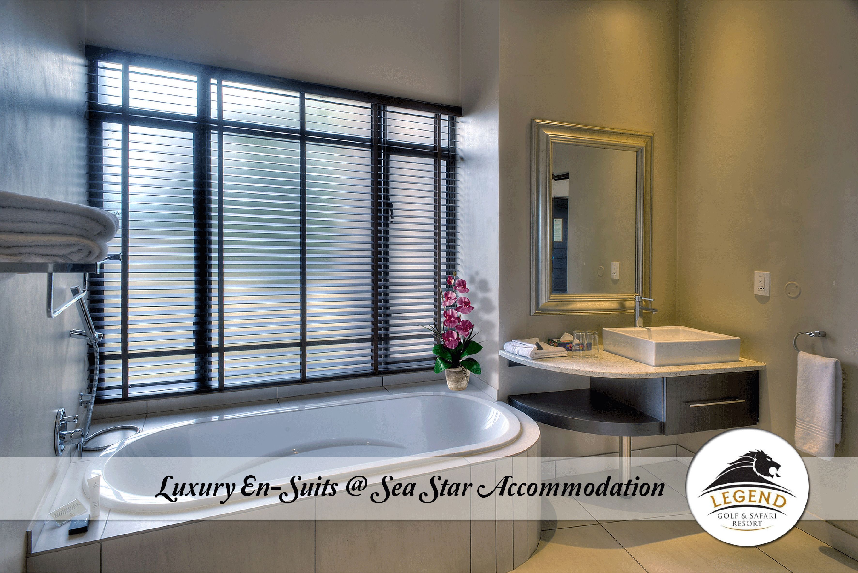 A modern bathroom with a large bathtub, a vanity with a mirror, and a window with blinds.