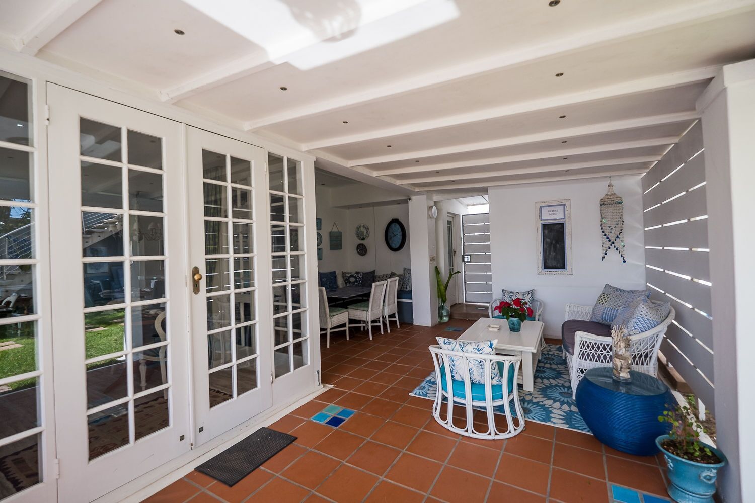 A spacious patio with a dining area, white wicker furniture, and a tiled floor.