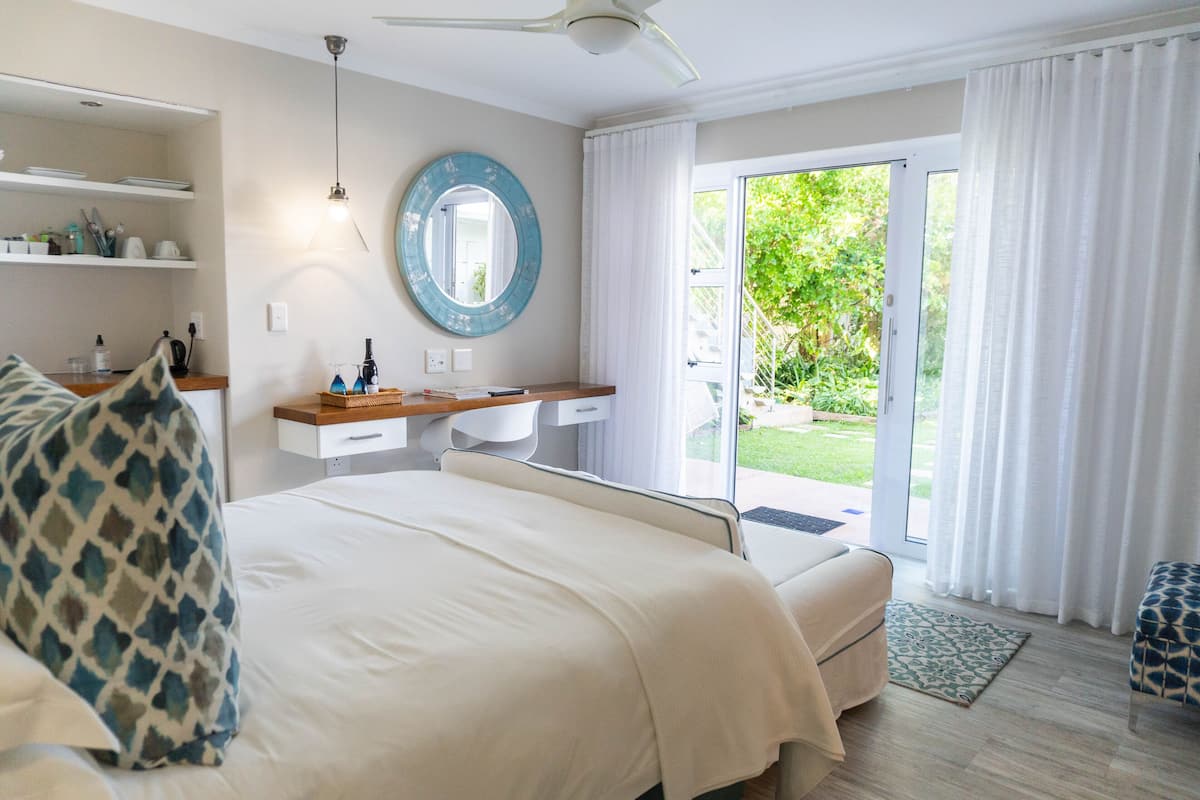 Ein Schlafzimmer mit Bett, Nachttischen, einem Spiegel und Blick ins Freie durch eine Schiebetür.