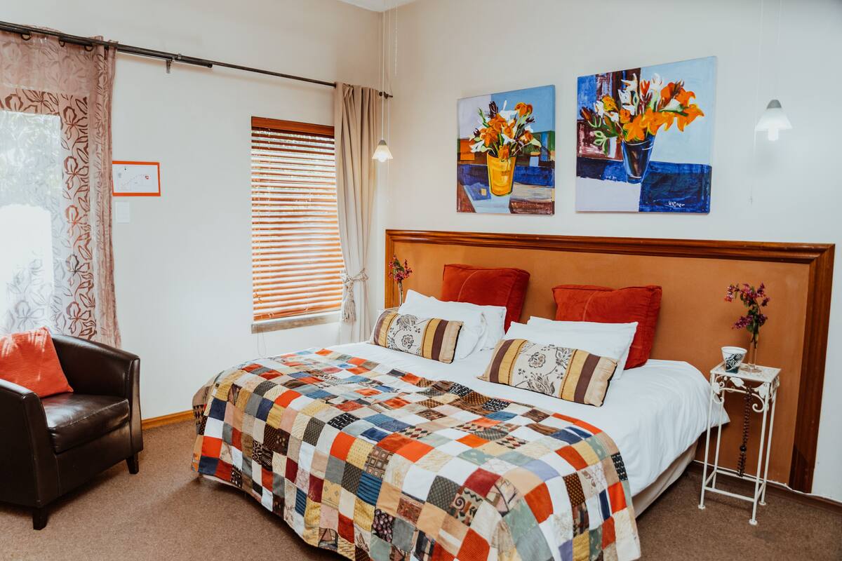 Ein Schlafzimmer mit einem großen Bett, einem hölzernen Kopfteil, einer Steudecke, einem Nachttisch, einer Lampe, einem Sessel und zwei Bildern an der Wand.