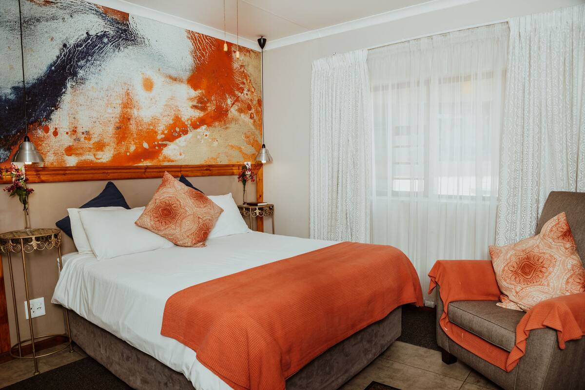Ein Hotelzimmer mit einem großen Bett, einem Sessel, einem Nachttisch und einem Bild an der Wand.