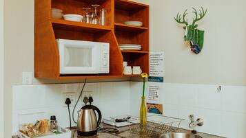 A kitchen with a microwave, shelves with dishes, a sink, and a decorative deer head.