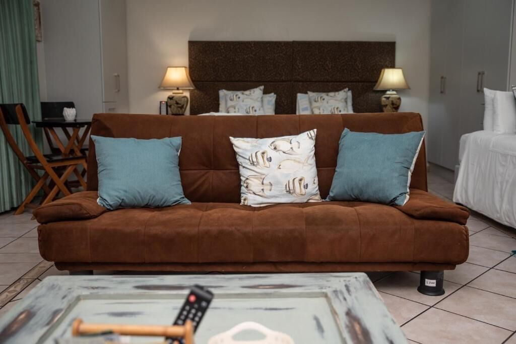 A brown sofa with two blue pillows, a remote control, and a decorative item on a coffee table.