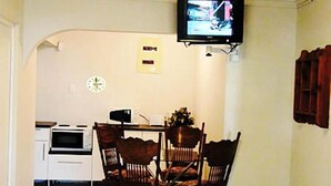 A dining area with a table and chairs, a television mounted on the wall, a clock, and a microwave. - Bluewater Reservations (Gqeberha (Port Elizabeth))