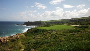 A coastal landscape with a golf course, ocean, and buildings.