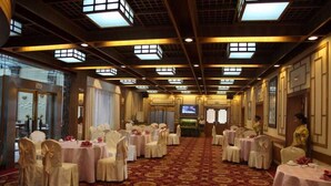 Un salón de banquetes con mesas redondas y sillas, una alfombra estampada y una pantalla de televisión.