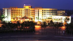Un hotel de varios pisos con un atrium central, palmeras en primer plano y señalización iluminada.
