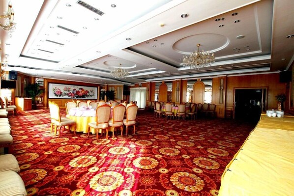 Un amplio salón de banquetes con alfombra estampada, mesas redondas con sillas y una araña.