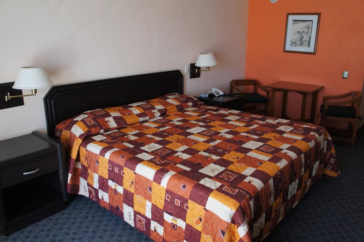 Ein Hotelzimmer mit einem Bett, zwei Nachttischlampen, einem Schreibtisch und einem Stuhl.