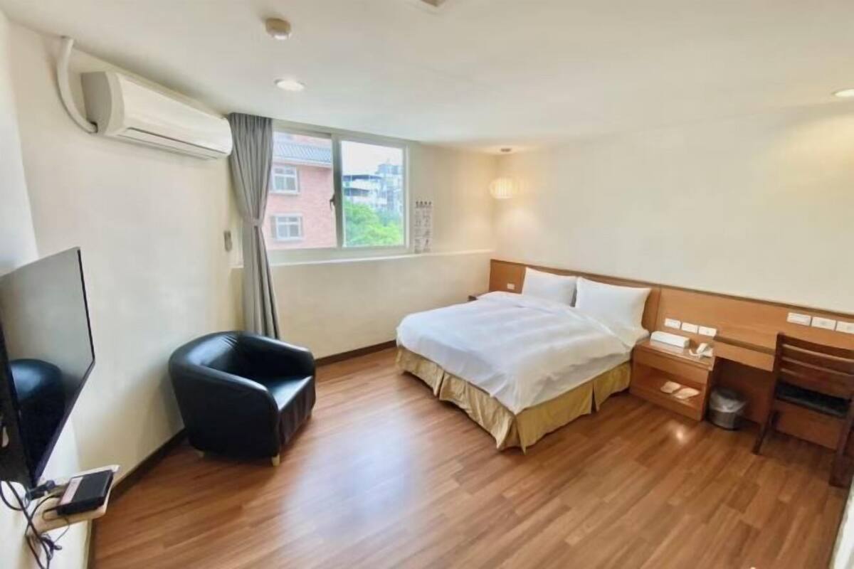 A hotel room with a bed, a TV, a chair, a desk, and a window.
