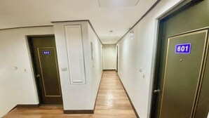 Corredor de hotel com piso de madeira, portas numeradas 605 e 601, e uma parede branca lisa.