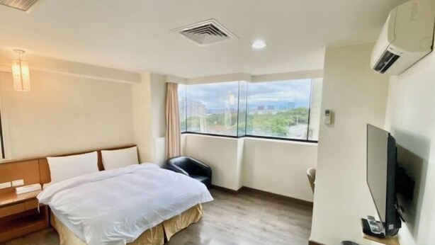 Quarto de hotel com cama, televisão, janela com vista e um respiradouro no teto.
