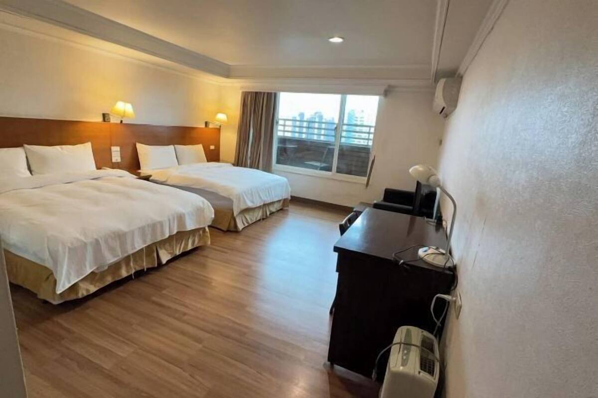 A hotel room with two beds, a desk, a chair, and a window with a view.