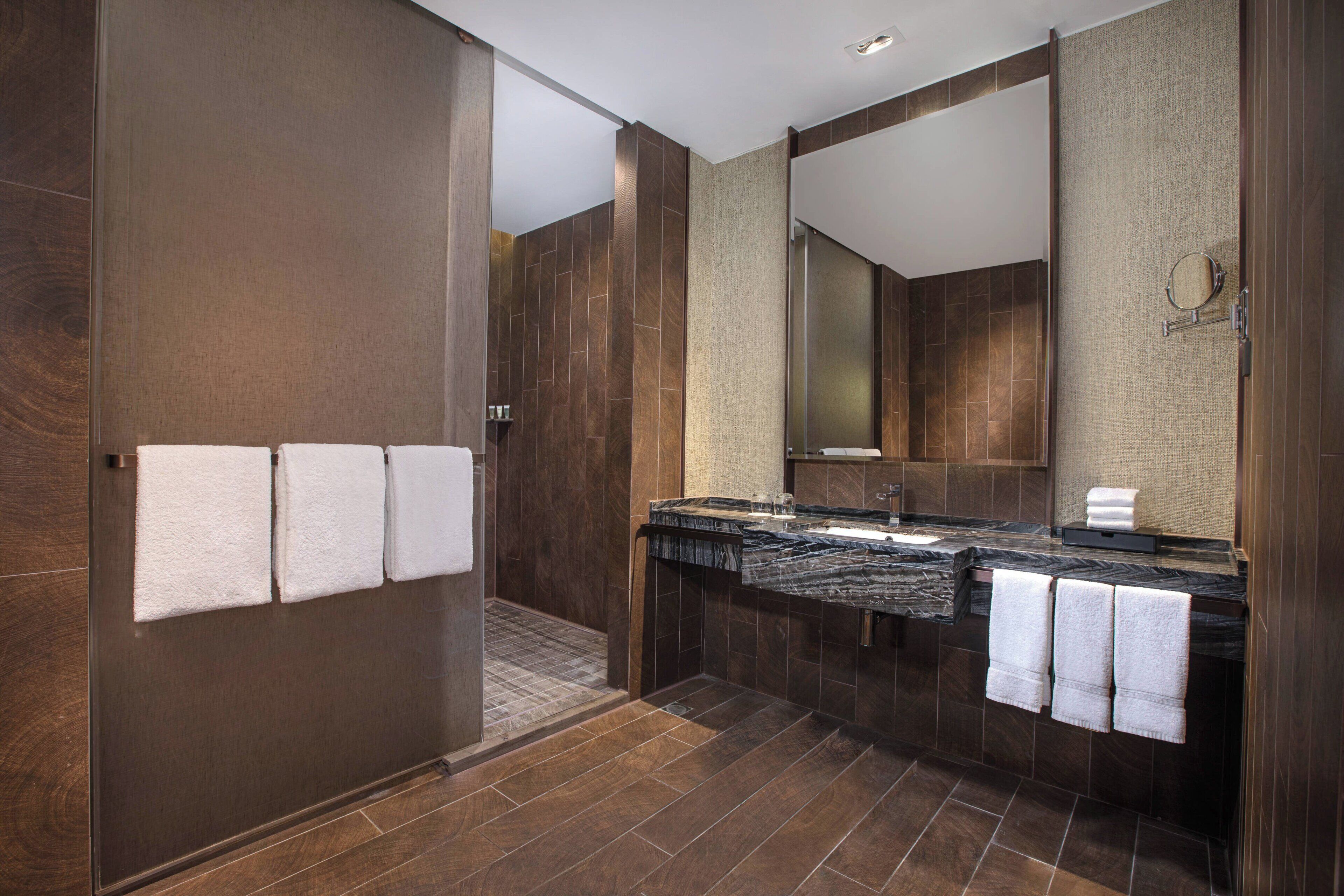 A modern bathroom with a walk-in shower, a large mirror, and a marble countertop.