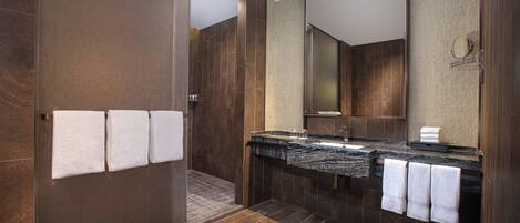 A modern bathroom with a walk-in shower, a large mirror, and a marble countertop.