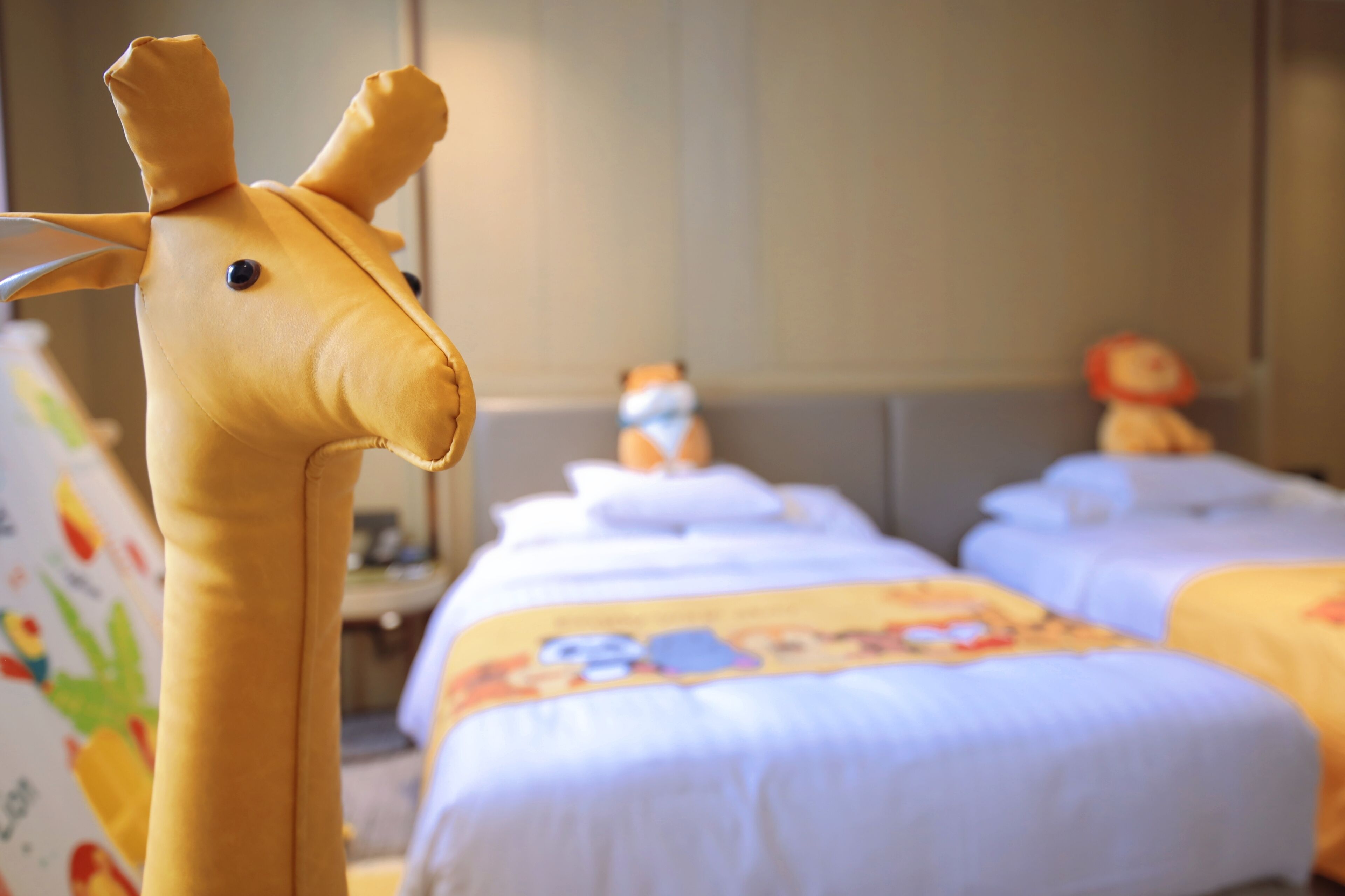A hotel room with a giraffe plush toy on the left, a bed with a cartoon character bedspread, and a teddy bear on the right.